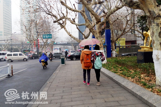 今日的杭州天降小雨，风速增大，路上行人正打着伞。