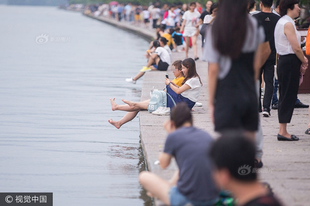 7月1日，杭州西湖白堤，许多游客脱掉了鞋袜，把脚伸进西湖里，洗脚、泡脚或戏水。